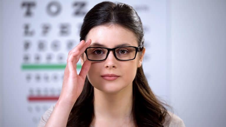 Woman tries on new glasses at an eye clinic in front of a eye exam chart