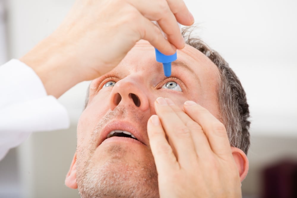Middle aged man uses eye drops to lubricate his eyes and relieve chronic dry eye symptoms.