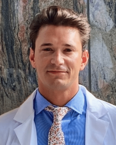Professional headshot of Dr. Luis Ortiz, OD, optometrist at St. Michael’s Eye & Laser Institute, wearing a white coat, blue shirt, and floral tie.