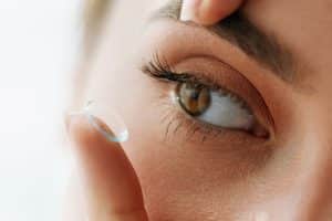 Woman puts contact lens in her eyes, hoping to avoid dry eye symptoms