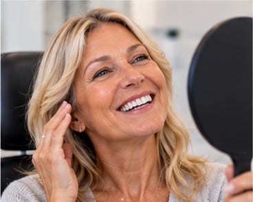 Smiling patient checking her vision in a hand mirror after LASIK